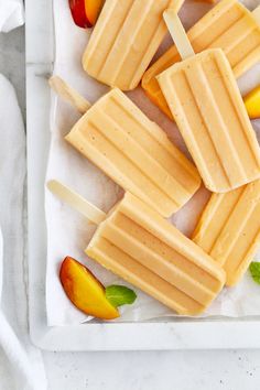 three popsicles on a plate with peaches and mint leaves next to them, ready to be eaten