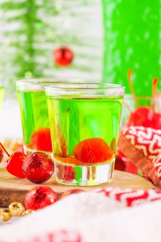 two glasses filled with green liquid next to cherries on a cutting board and candy canes