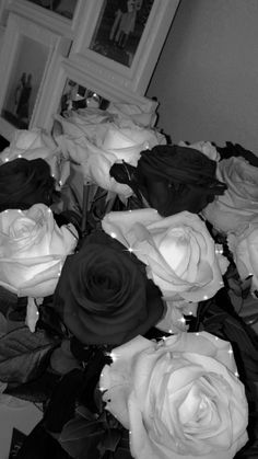 black and white roses in a vase on a table next to a mirror with framed pictures behind them