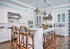 a large kitchen with white cabinets and wooden flooring, along with bar stools