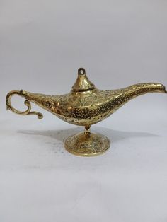 an antique brass teapot on a stand with a handle and foot rests against a plain white background