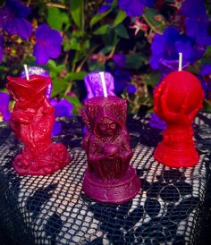 three red candles sitting on top of a table next to purple flowers