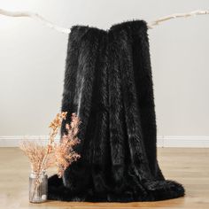 a black furry blanket sitting on top of a wooden floor next to a vase with dried flowers