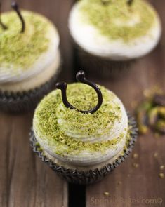 three cupcakes with frosting and green sprinkles sitting on a wooden table