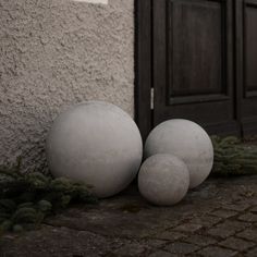 three white balls sitting on the ground next to a wall and door with moss growing around them