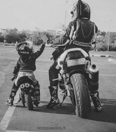 a man and child on a motorcycle in a parking lot with their hands up to each other