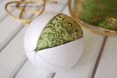 an ornament is sitting on top of a white ball with green and gold designs