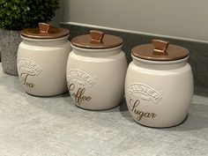 three white jars with brown lids sitting on a counter