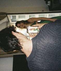 a man looking at his cell phone in front of an open refrigerator with two women