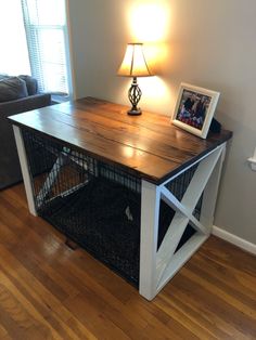 a wooden table with a cage underneath it on top of a hard wood floor next to a lamp