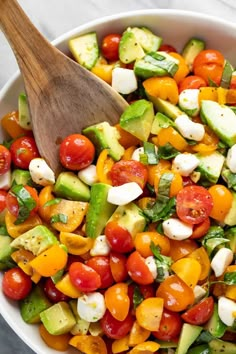 a white bowl filled with cucumber, tomato and avocado salad next to a wooden spoon