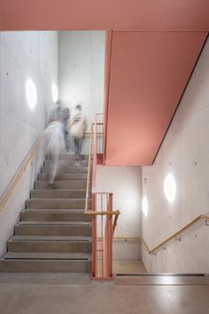 people walking up and down the stairs in a building with pink paint on the walls