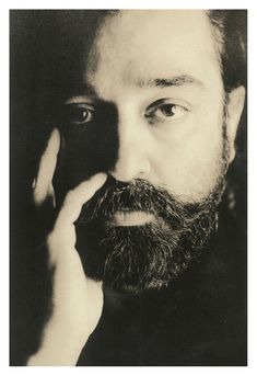 a black and white photo of a man with a beard holding his hand to his face