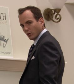 a man in a suit and tie standing next to a wall with a sign on it