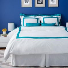 a bedroom with blue walls, white bedding and two framed pictures on the wall