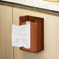 a brown tissue dispenser mounted to a wooden cabinet with white paper on it