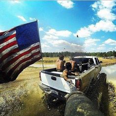 two men riding in the back of a pick up truck with an american flag on it