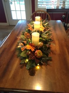 a wooden table topped with two candles and christmas wreaths on top of each other