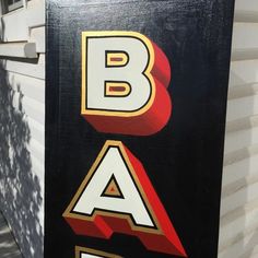 a black sign with red and yellow letters on it's side next to a building