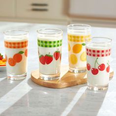 four glasses with fruit designs on them sitting on a counter top next to a plate