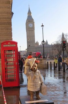 a statue of a teddy bear wearing a coat and hat in front of a red phone booth