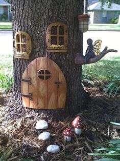 a tree with some little fairy houses on it's side and mushrooms in the grass