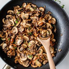 mushrooms are being cooked in a skillet with a wooden spoon