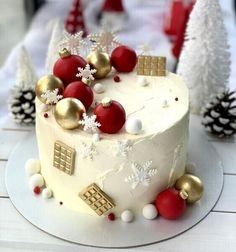 a white cake with red and gold decorations on the top is surrounded by pine cones