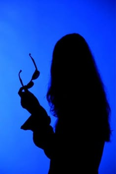 the silhouette of a woman holding a pair of scissors in her hand, against a blue background