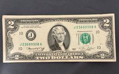 the two dollar bill is on display in front of a black background with white writing