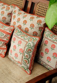 four decorative pillows on a bench with a plant in the corner and one cushion has an orange flower design