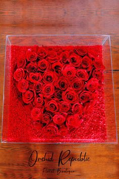 a clear box filled with red roses on top of a wooden table