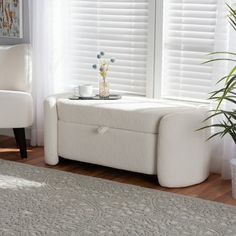 a white ottoman sitting in front of a window next to a chair and potted plant