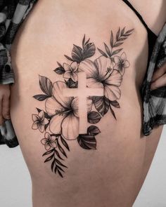 a cross and flowers tattoo on the back of a woman's thigh, with leaves around it