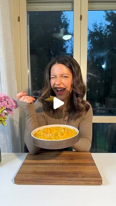 a woman holding a bowl of food in front of her face and eating it with a spoon