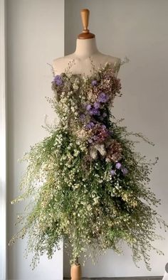 a mannequin covered in flowers and greenery next to a vase filled with baby's breath