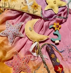 several handmade stars and moon decorations on a pink fabric material with gold sequins