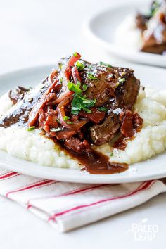 a white plate topped with mashed potatoes covered in meat and gravy on top of it