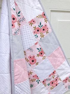 a pink and white quilt hanging from the side of a door with flowers on it