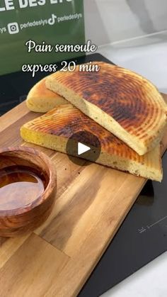 a wooden cutting board topped with two pieces of bread next to a bowl of dipping sauce