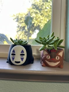 two planters sitting on top of a window sill next to a cat face