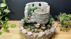 there is a rock fountain with rocks and plants in it on the table next to a potted plant