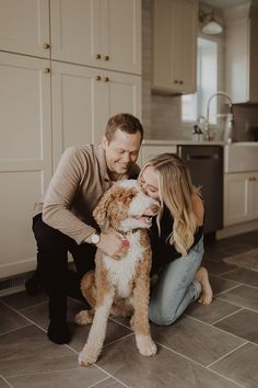 a man and woman petting a dog on the floor in front of their kitchen