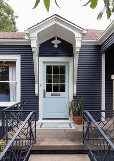 a blue house with stairs leading to the front door and potted plants on either side