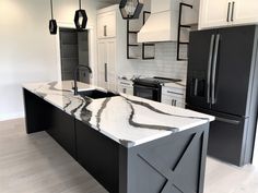 a kitchen with marble counter tops and black refrigerator freezer next to an island in the middle