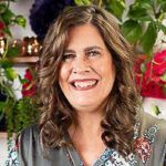 a woman with long hair smiling in front of some potted plants and other flowers