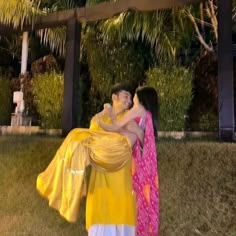 two women in sari hugging each other outside at night with palm trees behind them