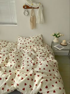 an unmade bed with red hearts on it in a bedroom next to a window