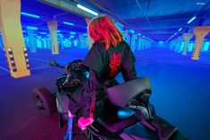 a woman riding on the back of a motorcycle in an underground parking lot with neon lights