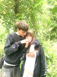 a young man and woman embracing each other in front of some trees with green leaves